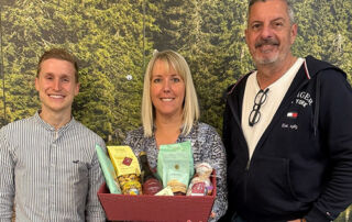 15 Jahre zuverlässige Partnerschaft: Tim Bauert, Monika Schäfer und Joachim Schäfer bei der Übergabe eines Geschenkekorbs